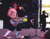 a shirtless man playing a guitar and singing into a microphone on a stage