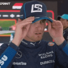 a man wearing a williams racing hat adjusts it