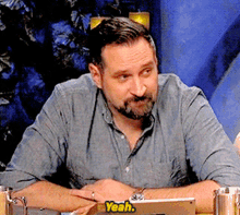 a man with a beard is sitting at a table with a tablet and a sticker that says yeah
