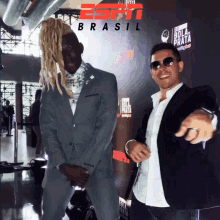 a man in a suit stands next to another man in front of a sign that says espn brasil