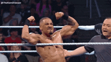 a wrestler is flexing his muscles in a wrestling ring while a referee looks on