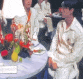 a man in a white shirt is sitting at a table with flowers on it .