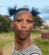 a man with pigtails and a nose ring is standing in a field and making a funny face .
