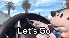 a stuffed mickey mouse is driving a car with the words let 's go on the steering wheel