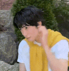 a young man in a yellow vest and white shirt is sitting on a rock .