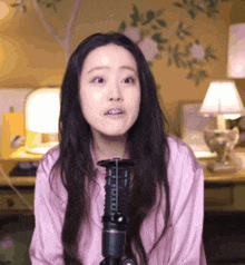 a woman in a pink shirt stands in front of a black microphone