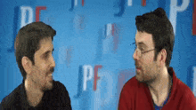 two men are having a conversation in front of a blue background with letters pf on it