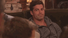 a man is sitting on a couch with a group of people and looking at the camera .