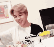 a man is laughing while sitting at a table with a plate of food .