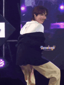 a man in a black and white jacket is dancing on a stage with purple lights behind him