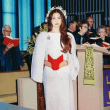a woman in a white dress stands in front of a podium holding a red book