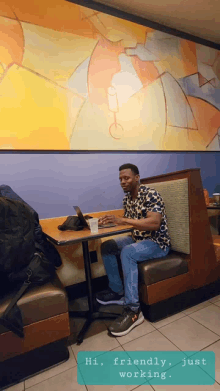 a man sits at a table with a laptop and a cup of coffee and says " hi friendly just working "