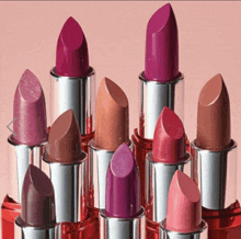 a bunch of lipsticks are stacked on top of each other on a pink background