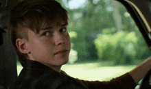 a young boy is sitting in the driver 's seat of a car and looking at the camera .
