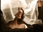 a woman in a wedding dress is smiling with her veil covering her face