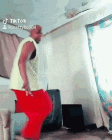 a man in a yellow shirt and red pants is dancing in a living room with tiktok written on the bottom