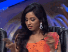 a woman in an orange dress is sitting in a chair with the word ruby on the bottom right
