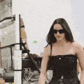 a woman wearing sunglasses and a black dress is standing in front of a wall .