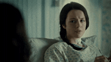 a woman in a hospital gown sits on a couch
