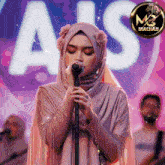 a woman in a hijab singing into a microphone in front of a sign that says ais