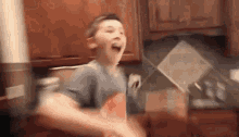 a young boy is standing in a kitchen with his mouth open and holding a bag of chips .