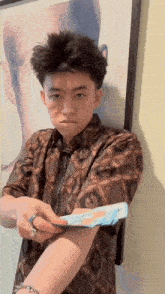 a young man in a brown shirt is holding a piece of paper in his hand