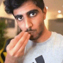 a man with a beard is wearing an adidas shirt and eating something