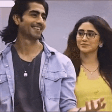 a man and a woman are standing next to each other and smiling . the woman is wearing glasses and a yellow top .