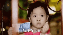 a little girl is holding a dollar bill with the name sabrina written on it
