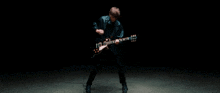 a man in a leather jacket is playing a guitar in a dark room