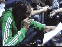 a man in a green adidas jacket sits on a couch holding a piece of paper