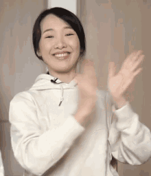 a woman in a white hoodie is smiling and clapping her hands