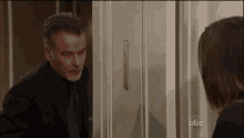 a man in a suit and tie is standing in a doorway talking to a woman .