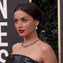 a woman wearing a necklace and earrings is standing in front of a sign that says ' hollywood ' on it