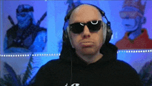 a bald man wearing sunglasses and headphones looks at the camera
