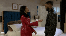 a man and a woman standing next to each other in front of a bed