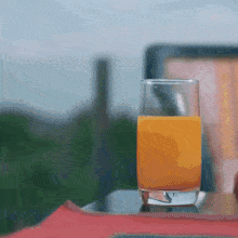 a glass of orange juice is on a table with a chair in the background .