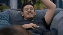a man is laying on a blue couch with his arms in the air .