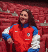 a woman wearing a red , white and blue nike jacket is sitting in an empty auditorium .