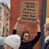 a man is holding a sign that says actually 98.4% of human history is older than stonehenge