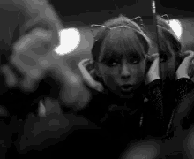 a black and white photo of a woman wearing cat ears looking at her reflection in a mirror .