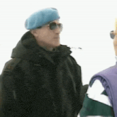 a man wearing a blue beret and sunglasses is standing in the snow