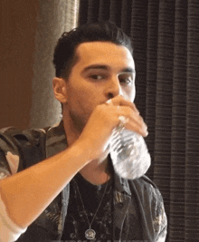 a man drinking water from a bottle with a necklace around his neck