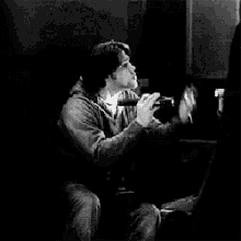 a black and white photo of a person sitting in a dark room with a light shining on them .