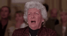 an elderly woman with gray hair is making a funny face in front of a crowd .