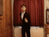 a man in a suit is dancing in front of a window with red curtains