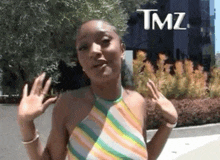 a woman in a striped top is waving her hand in front of a building that says tmz