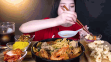a woman is eating a bowl of food with chopsticks and a spoon
