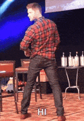 a man in a plaid shirt and black jeans is standing on a stage with his hands in his pockets .
