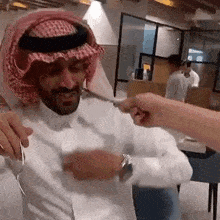 a man wearing a keffiyeh and a white shirt is being touched by another person .